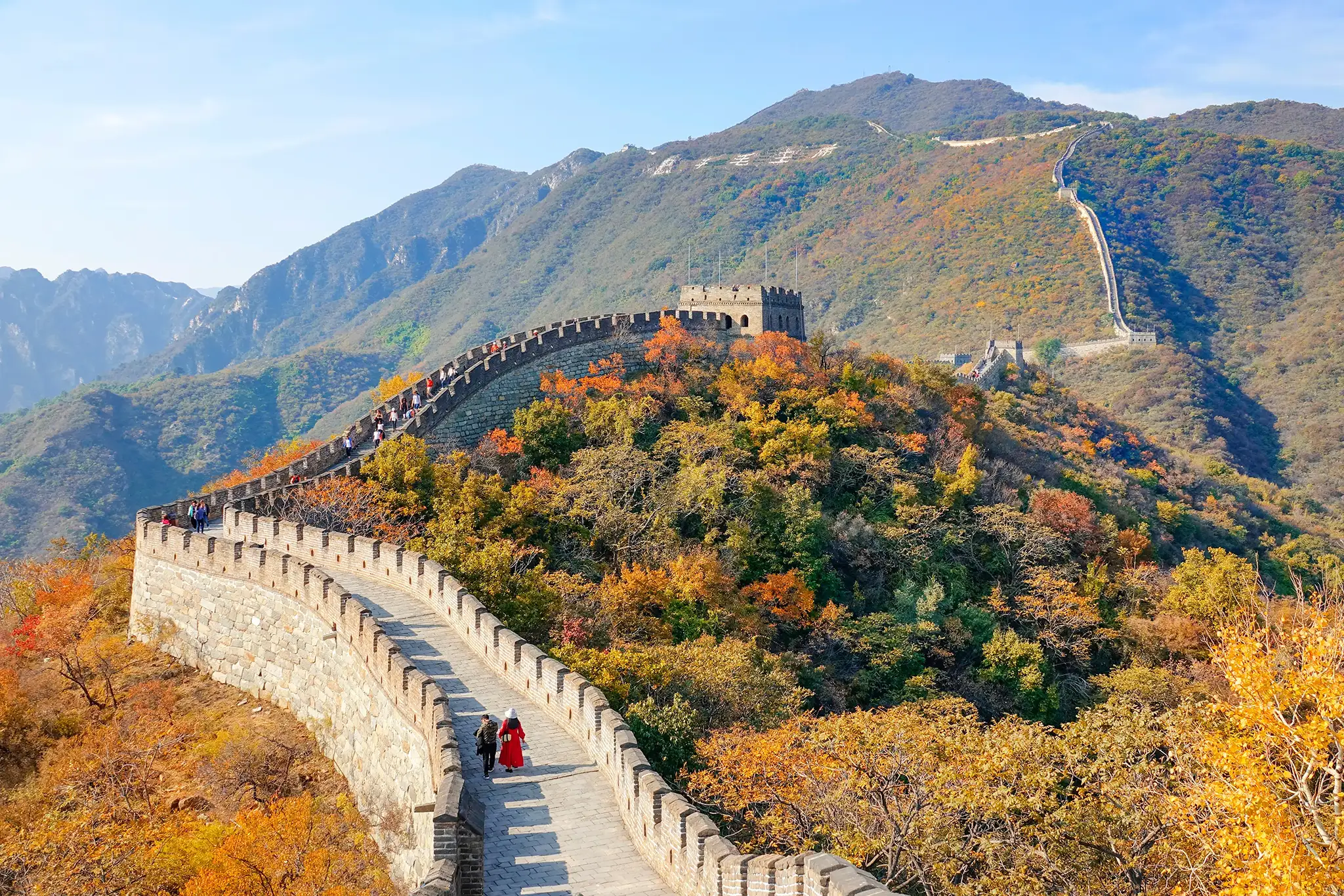 Two unrecognisable tourists walk along the walkway atop the Great Wall of China.