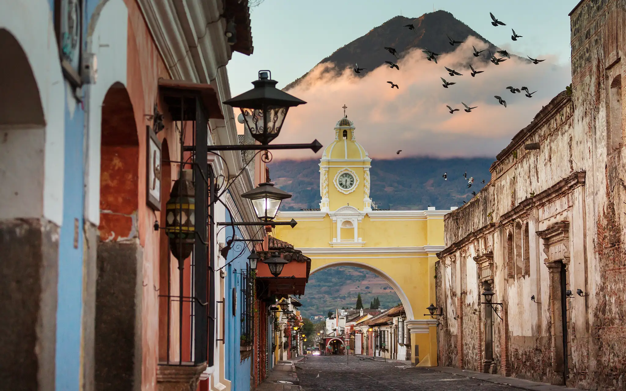 Cityscape of the main street and yellow Santa Catalina arch in the historic city center of Antigua at sunrise with the Agua volcano, Guatemala.