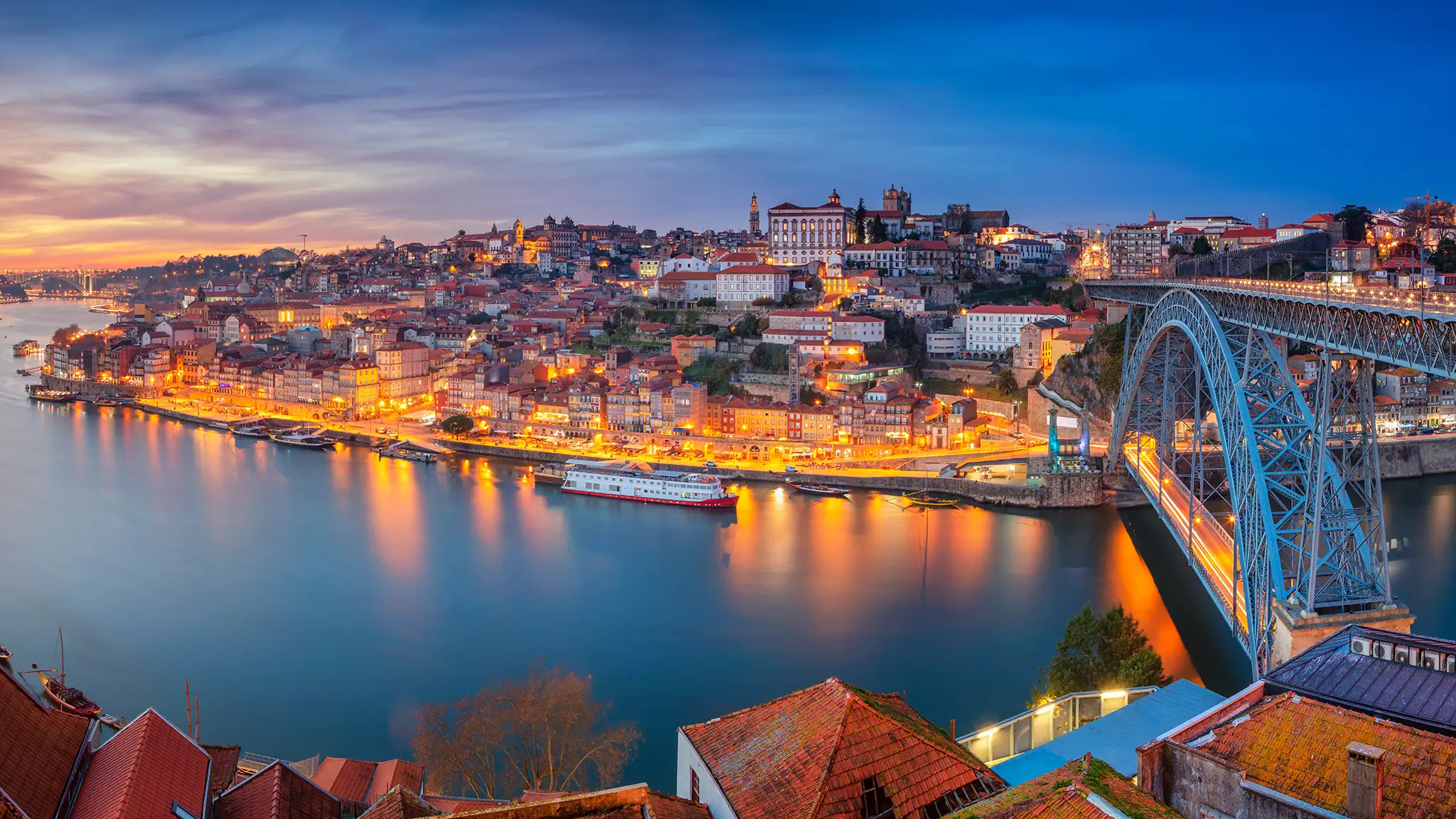 Panoramic cityscape image of Porto, Portugal with the famous Luis I Bridge and the Douro River during dramatic sunset.