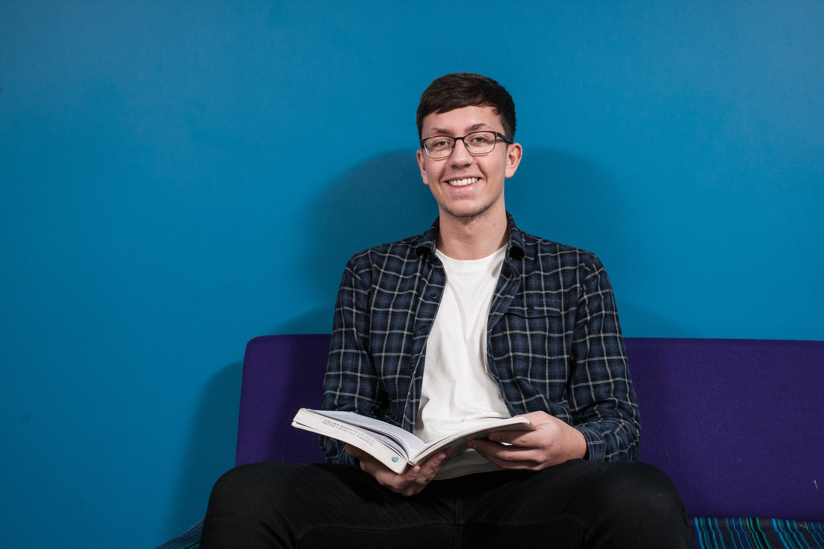 A male student sitting directly in front of camera, smiling and holding a book.
