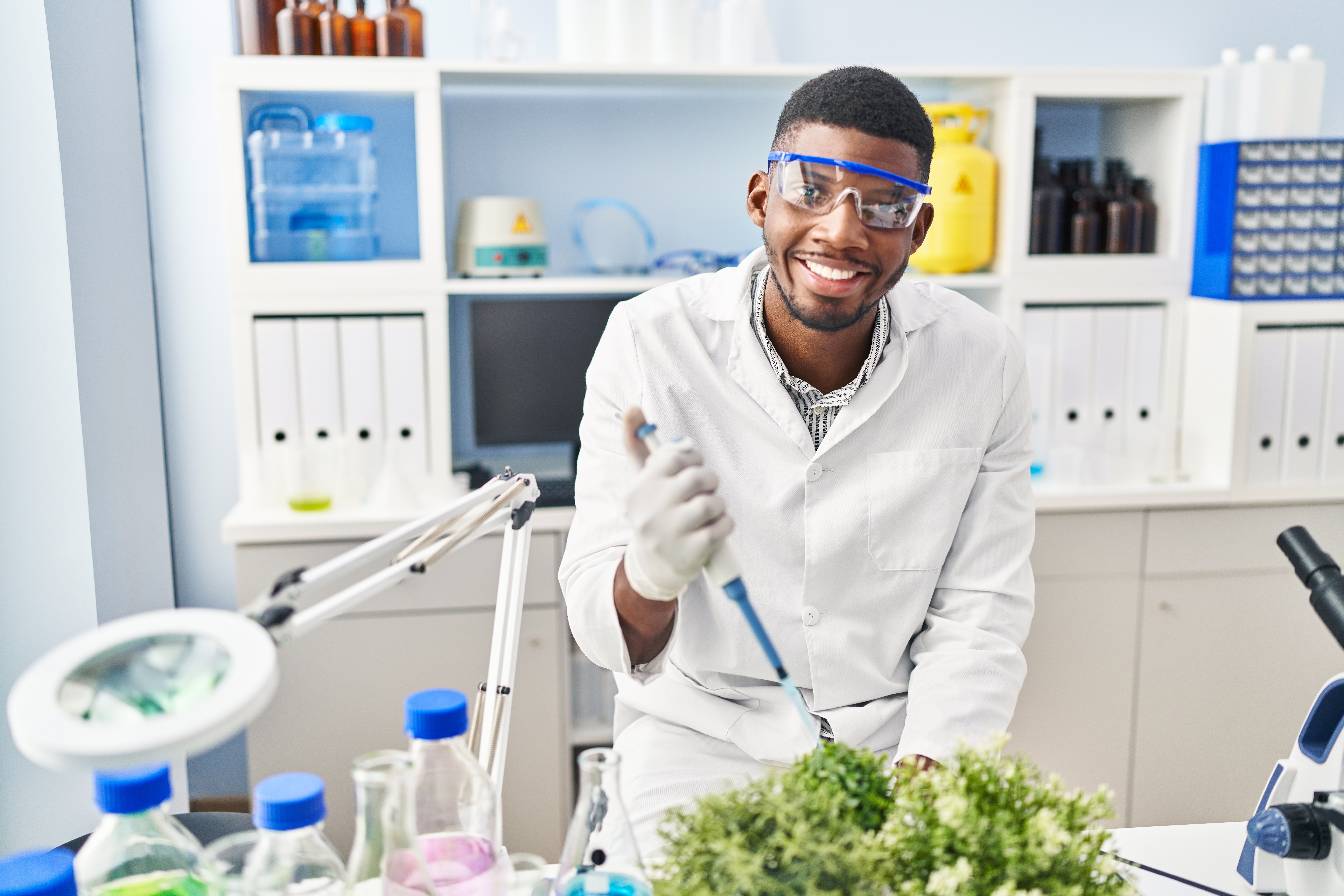 Young african american man wearing scientist uniform using pipette on plant at laboratory