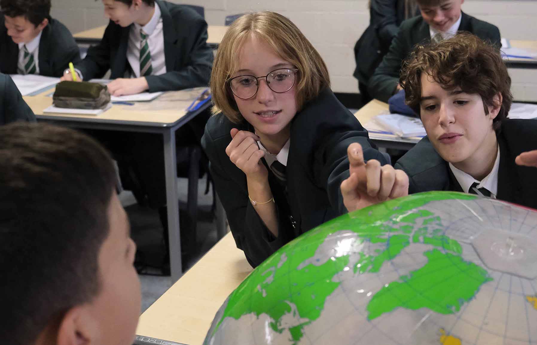 Students in a classroom looking at a large globe.