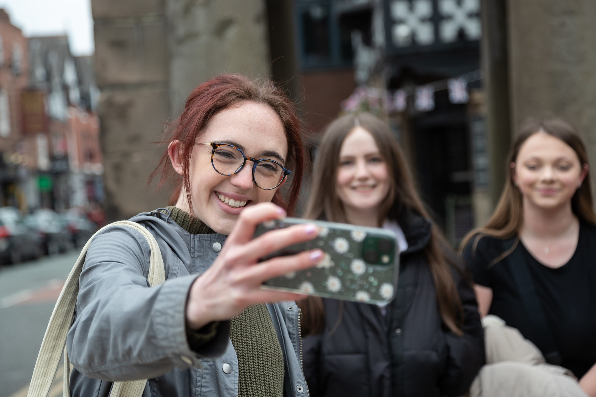 Female student holding her mobile phone taking a selfie with two other girls in the background