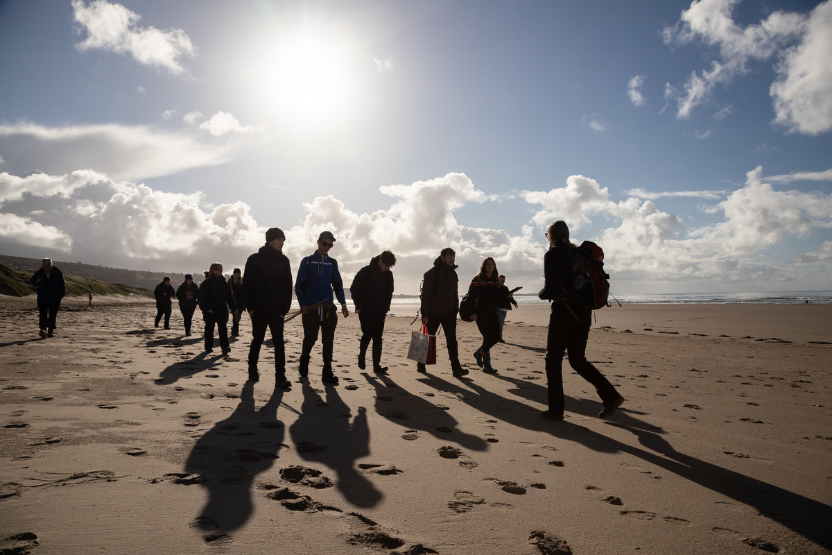 A group of people walking on seashore in brilliant sunshine.