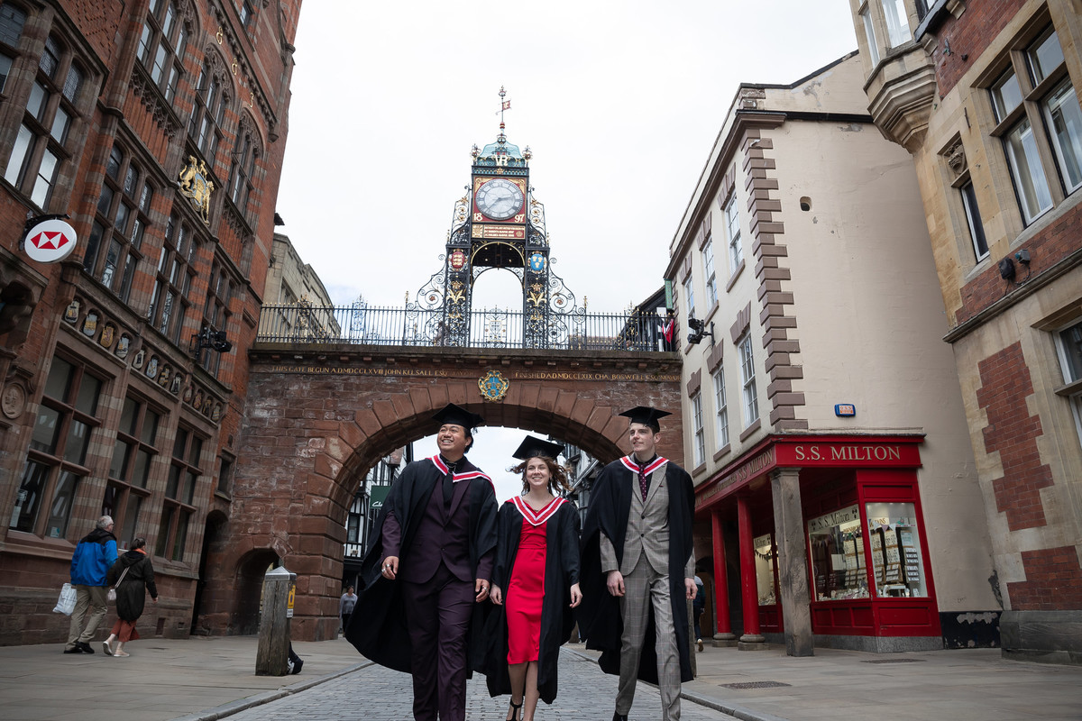 A group of people in graduation clothing walk under Eastgate Clock