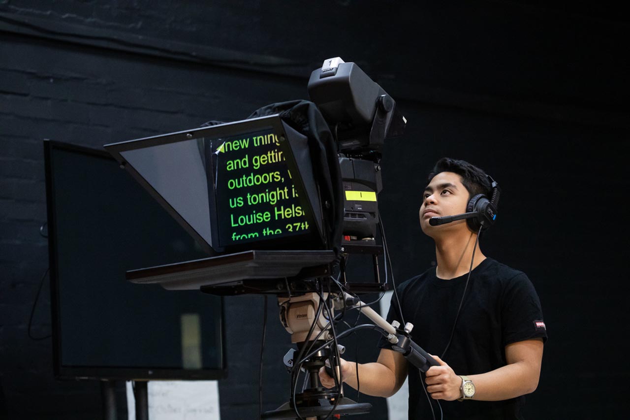 A student operating a  film media camera in a dark background studio room.