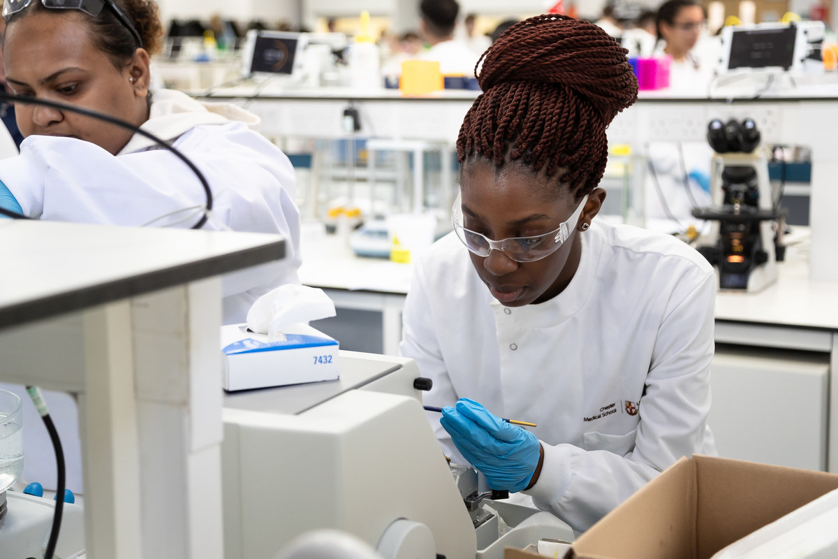 Students working a laboratory in wearing white coats and protective glasses.