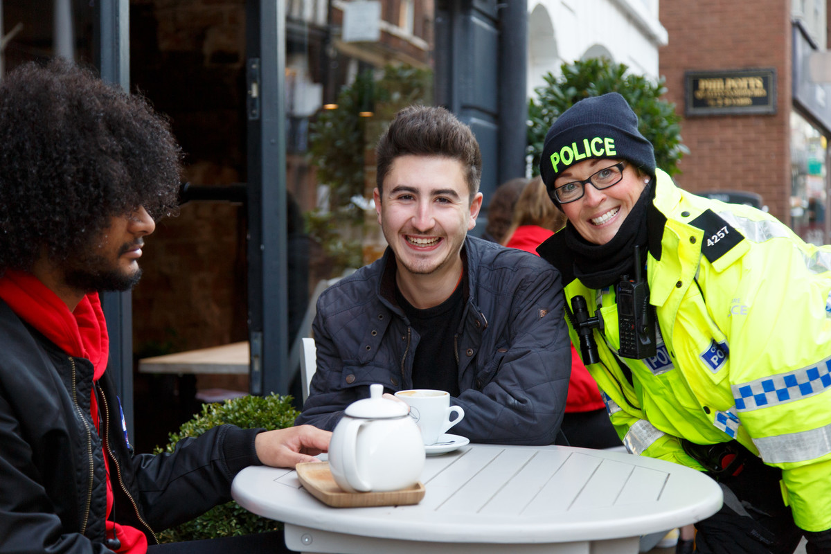 Students sitting at a table outside a cafe, talking with community police officer.