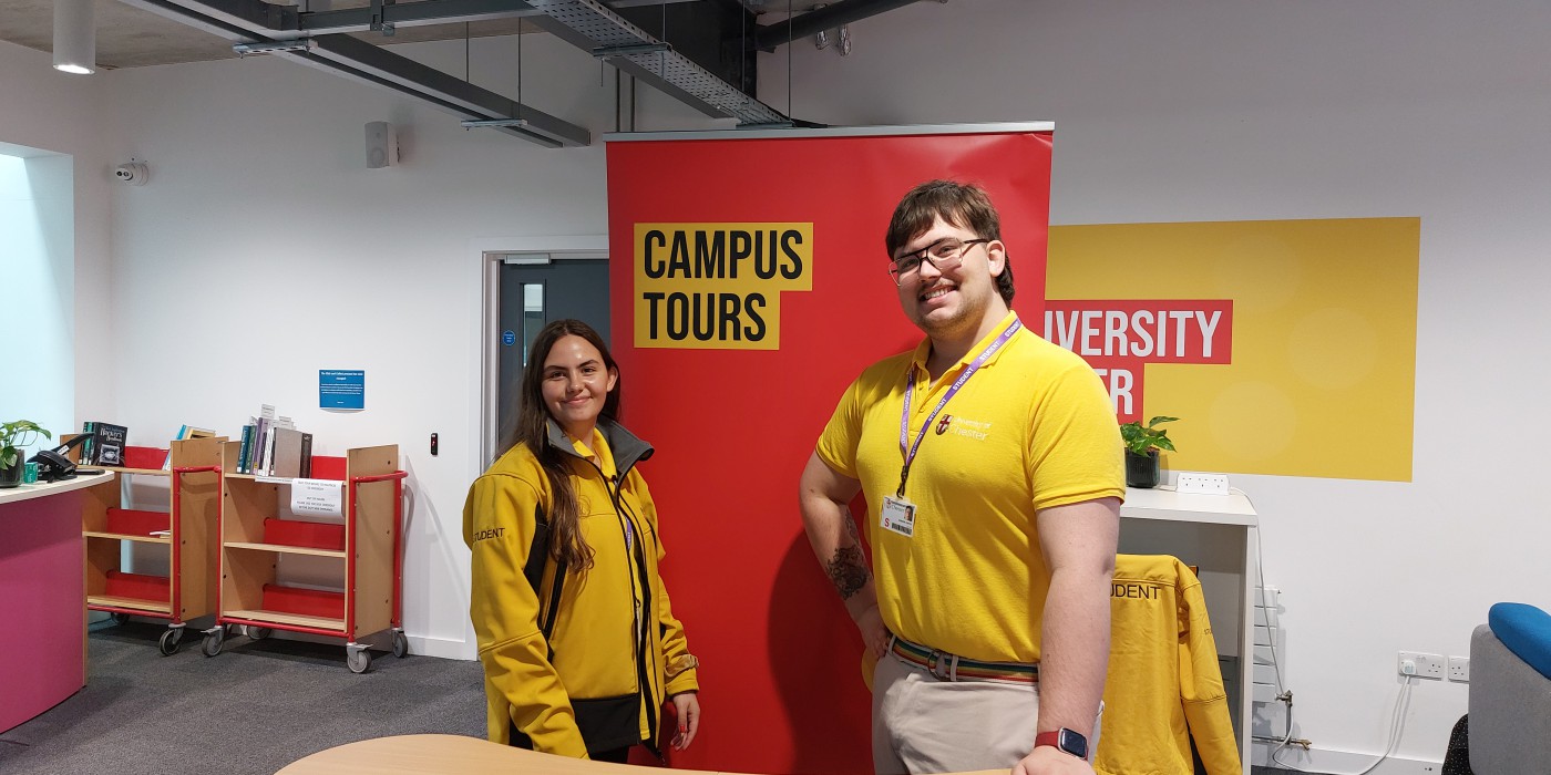 Two student ambassadors standing in front of a 'campus tours' sign