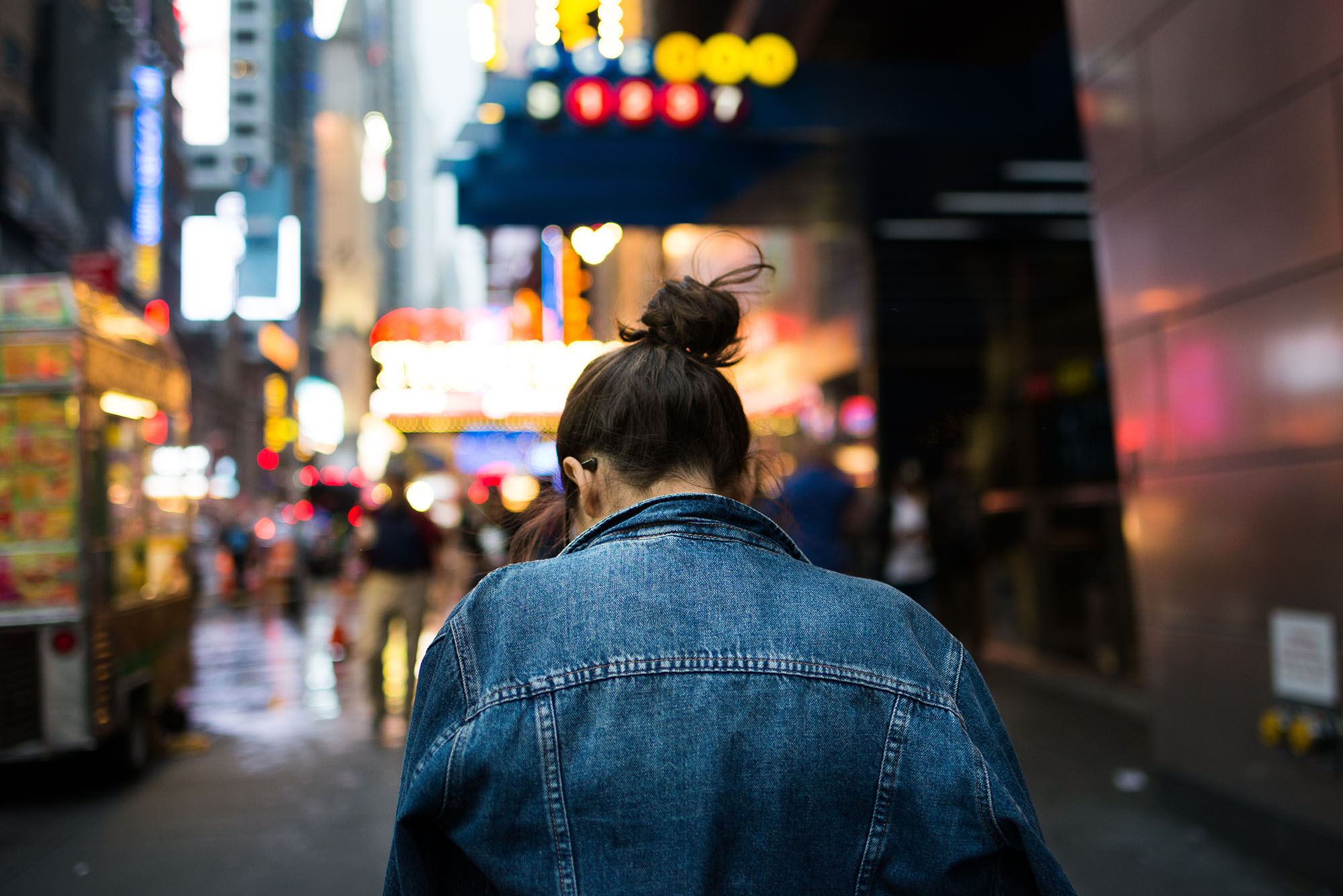 Person walking in New York City with bright signs and lights blurred in the background