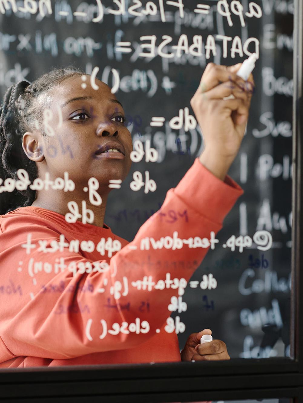 Black female teacher writing codes on blackboard