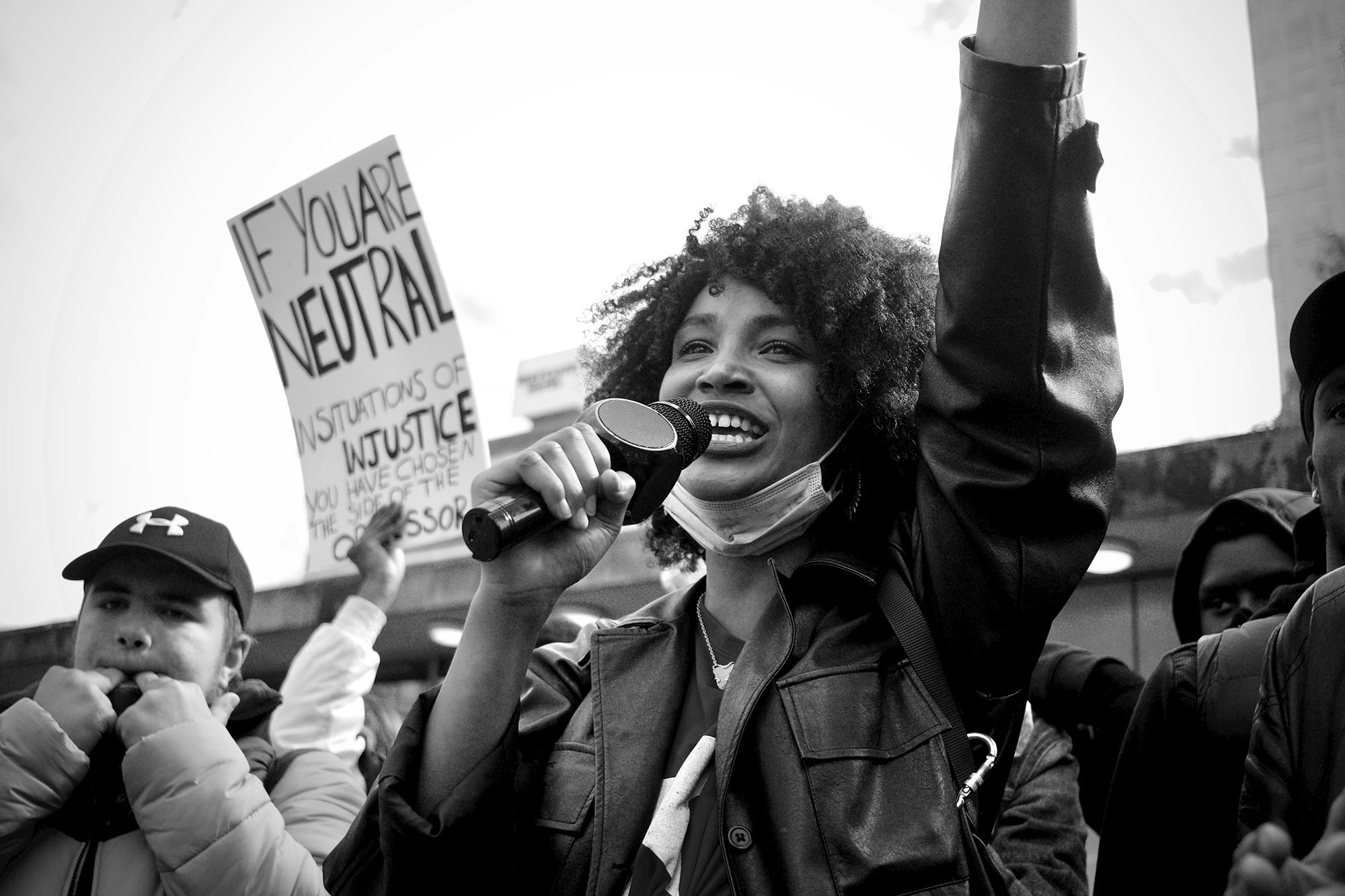 Greyscale photo of woman in black jacket holding microphone during a protest