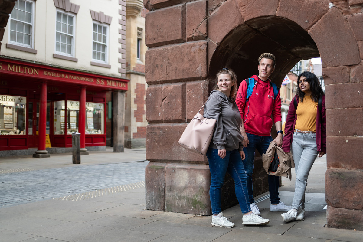 Two female and one male student walking in the street past city centre brick building.